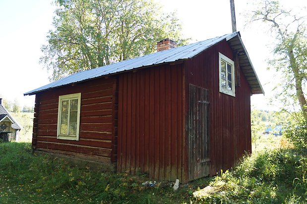 Vamsta 7:2. Stuga i rött timmer och panel, svart port och fönster med vita spröjs.