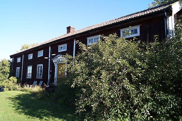 Åkre 1:5. Hus i två våningar i brun panel med fönster med vita spröjs, en gul dubbeldörr, en skorsten i tegel.