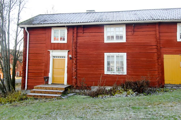 Lockne-Berge 2:2. Byggnad i rött timmer i två våningar, med fönster med vita spröjs, en liten trapp upp till en gul dörr och gul port.