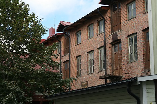 Tegelbyggnad i tre våningar, fönster i grönt med spröjs. Bruna portar.