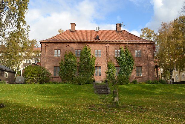 Tegelbyggnad i två våningar i brunt tegel. Bruna fönster och spröjs, brun dubbeldörr med fönster, två skorstenar.