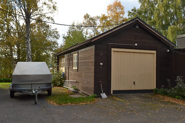 Byggnad i en våning i svart, liggande bred panel. En gul Garageport, en gul garageport med fönster och ett gult fönster med spröjs.