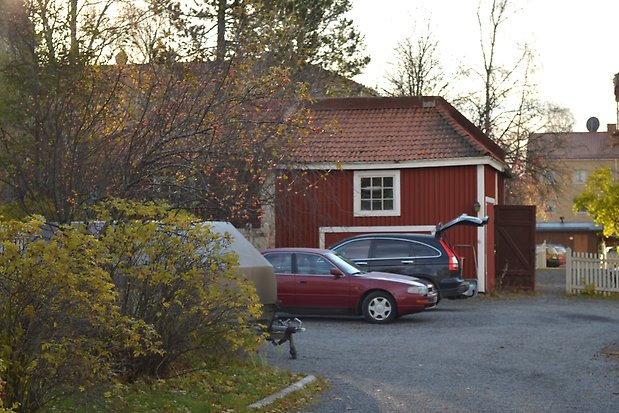 Byggnad i röd panel med vita knutar och fönsterfoder, vitt fönster med spröjs och många rutor, rött tegeltak.