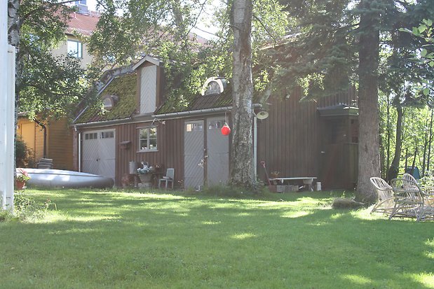 Byggnad i två våningar i brun panel. Två grå dörrar, en grå garageport på nedervåningen, och en grå dörr på andra våningen.