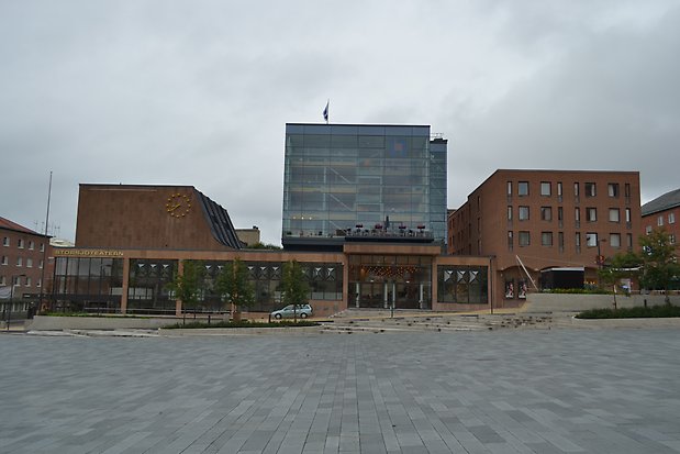 Byggnadolika våningshöjd i brun tegel. Guldklocka på fasaden. Stora glaspartier.