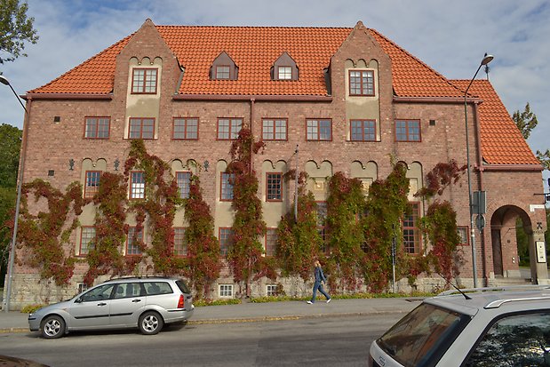 Byggnad i brunt tegel med orange tegeltak med stora och små takkupor. 