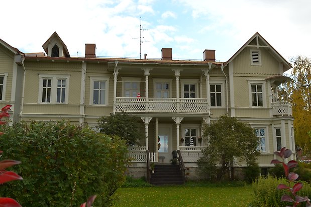 Trähus i tre våningar i beige, liggande panel med vita fönster med spröjs och vita och detaljer. balkong och veranda med snickarglädje. 