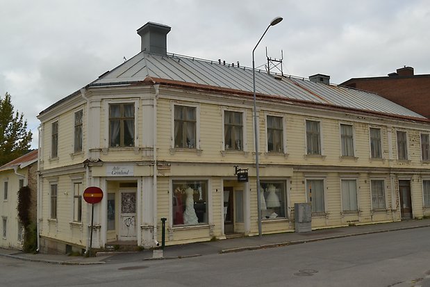 Träbyggnad i två våningar i ljusgul liggande panel, vita detaljer, vita fönster med gråbruna spröjs. Grått plåttak.