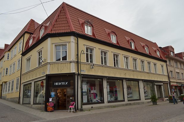 Hörnbyggnad i tre våningar, Träfasad i gult. Orange tegeltak med takkupor. Fönster med vita spröjs.