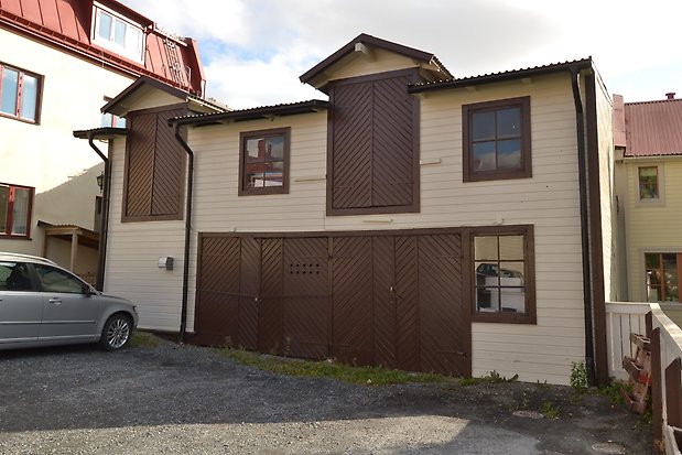 Uthus i två våningar, gul liggande panel med bruna portar och fönster med bruna spröjs och fönsterfoder.