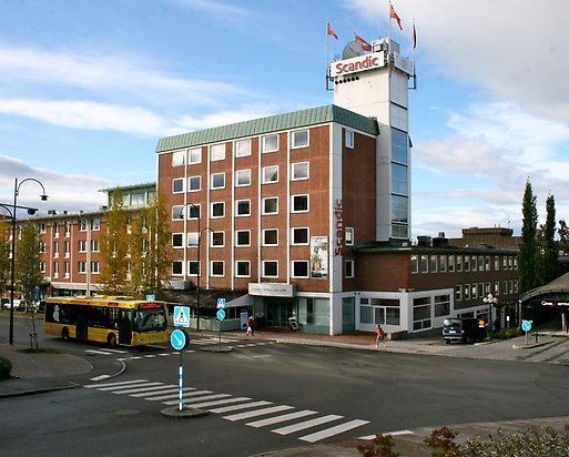 Hotellbyggnad i brunt tegel  med ett högre vitt, kantigt torn med skylt och flaggor.