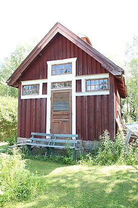 Näs-Åsen 3:18. Byggnad i röd panel med gul dörr och fönster med många småfönster.