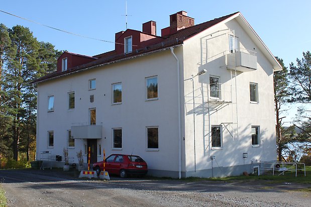 Valla 6:1. Byggnad i tre våningar i vit puts, vita fönster, balkong och metalltrappa på kortsidan, rött tegeltak med takkupor.