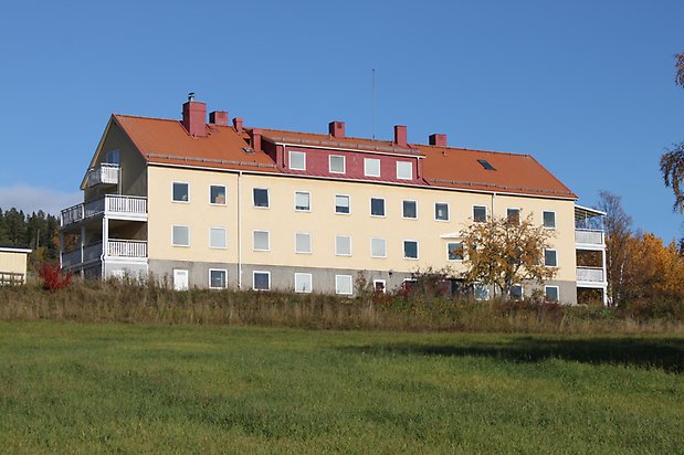 Valla 6:1. byggnad i tre våningar i ljusgul puts med vita fönster, rött tegeltak, veranda och balkonger i vitt på kortsidan.