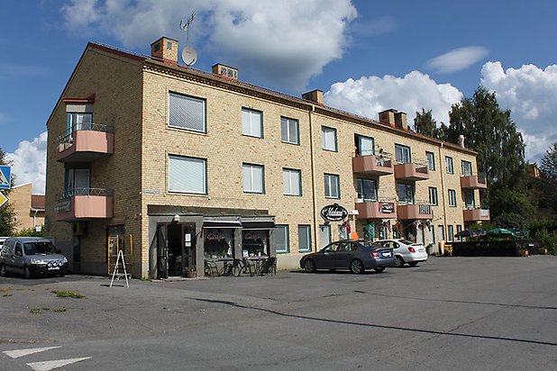 Bergsvik 9. Flerbostadshus i gult tegel i tre våningar med rosa balkonger och butikslokal på nedervåningen.