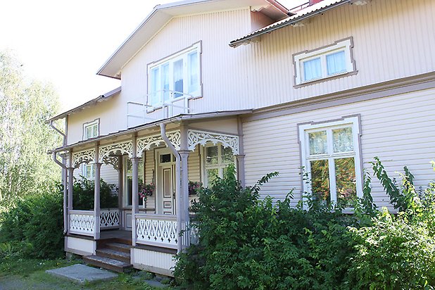 Söre 4:44. Villa i ljusbeige, liggande panel med mörkare detaljer och vita fönster med spröjs. Veranda i snickarglädje.