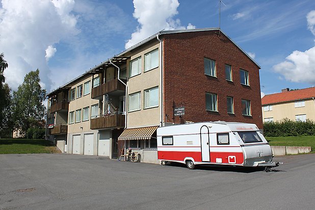 Söre 2:99. flerbostadshus i tre våningar i brunt tegel och beige puts, bottenvåningen har vita garageportar.