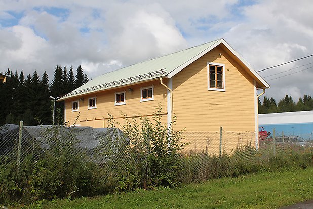 Söre 3:57. Byggnad i gul, liggande panel, brun dörr och små fönster.