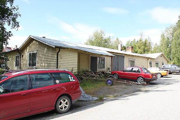 Tand 2:82. Byggnad i ljusgul, liggande panel med vita fönster.