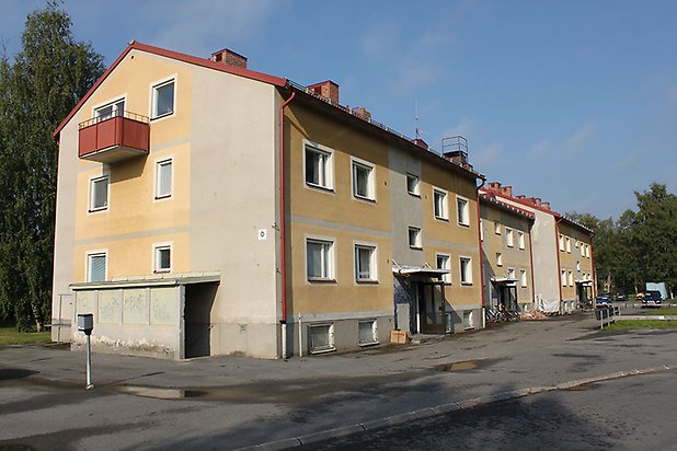 Tand 2:110. Flerbostadshus i gul och beige puts med vita fönster och röd balkong på kortsidan.