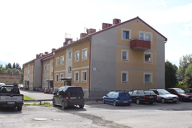 Tand 2:110. Flerbostadshus i gul och beige puts med vita fönster och röd balkong på kortsidan.