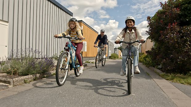 Två barn som cyklar till skolan med en förälder.