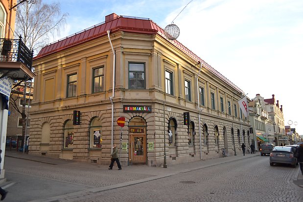 Hörnbyggnad i två våningar i sten. Rött plåttaket. Fönster i valv i markplan. 