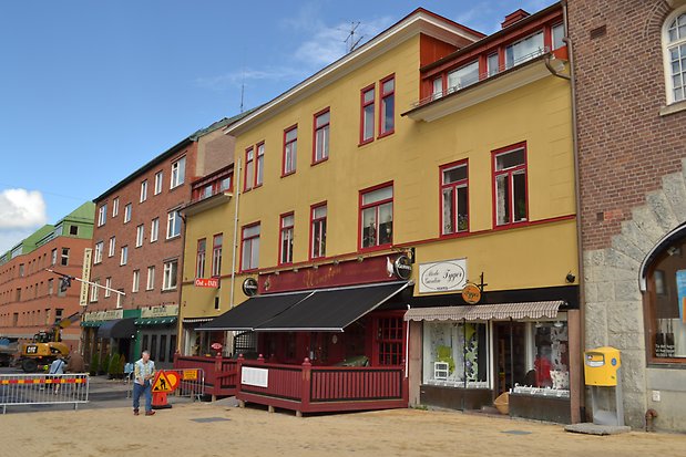 Stenbyggnad i trevåningar i senapsgul puts, röda detaljer och en mörkröd veranda.