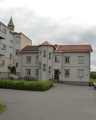 Träbyggnad i två våningar i ljusgrå, liggande panel med mörkgrå detaljer, Vita fönster, rött tak. Åttkantig utbyggnad för trapphuset mitt på byggnaden