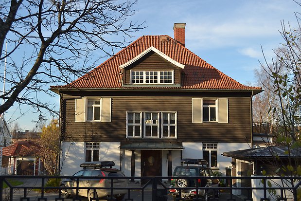 Villa i tre våningar, första våningen i vit puts, andra i brun liggande panel. Vita fönster med spröjs, lusbeige fönsterluckor. Orange tegeltak med takkupa, skorsten.