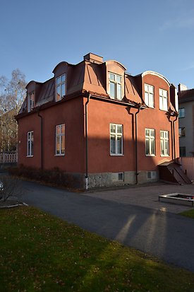 Stenhus i röd puts i två våningar. Stengrund och rött plåttak med takkupor. Vita fönster med spröjs.