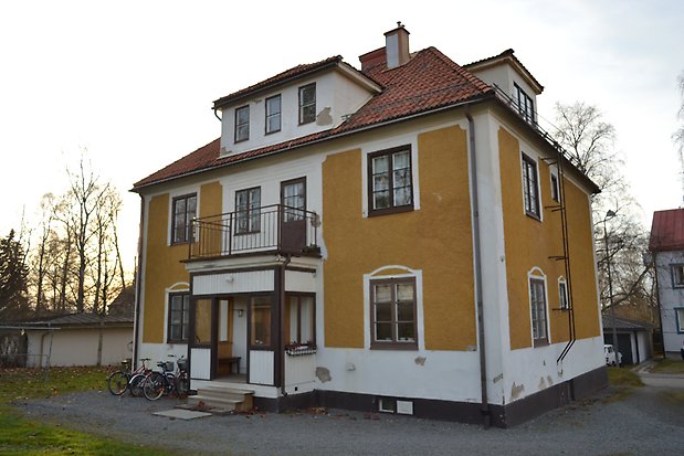 Stenhus i tre våningar i gul och vit puts. Bruna fönster med spröjs. Rött tegletak med två takkupor. Förstukvist med balkong över.