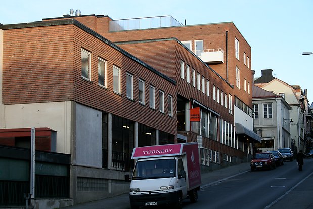 Brun tegelbyggnad i 2-4 våningar. Vita fönster. Skyltfönster i markplan. 