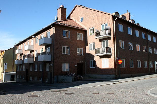 Byggnad i tre våningar i brunt tegel. Vita balkonger, och balkonger med svart räcke. Vita fönster utan spröjs, tegeltak.