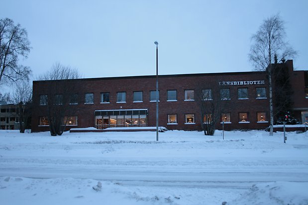 Brun tegelbyggnad i två våningar. Svarta fönster utan spröjs. Brett burspråk på markplan.