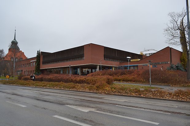 Tegelbyggnad i två plan. Höga, smala och tättsittande fönster på våning 2. Stora fönster partier på våning ett under utskjutande våning 2.