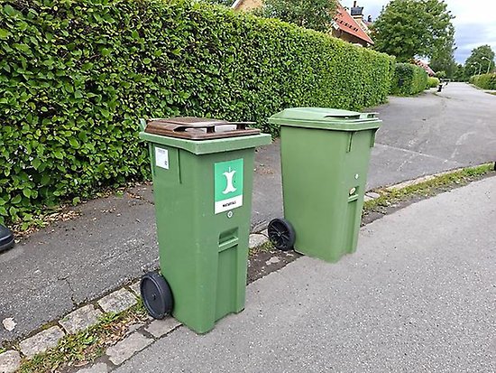 Två stoptunnor står med hjulen och draghandtaget vända från vägen. De står också ungefär en halvmeter ifrån varandra.